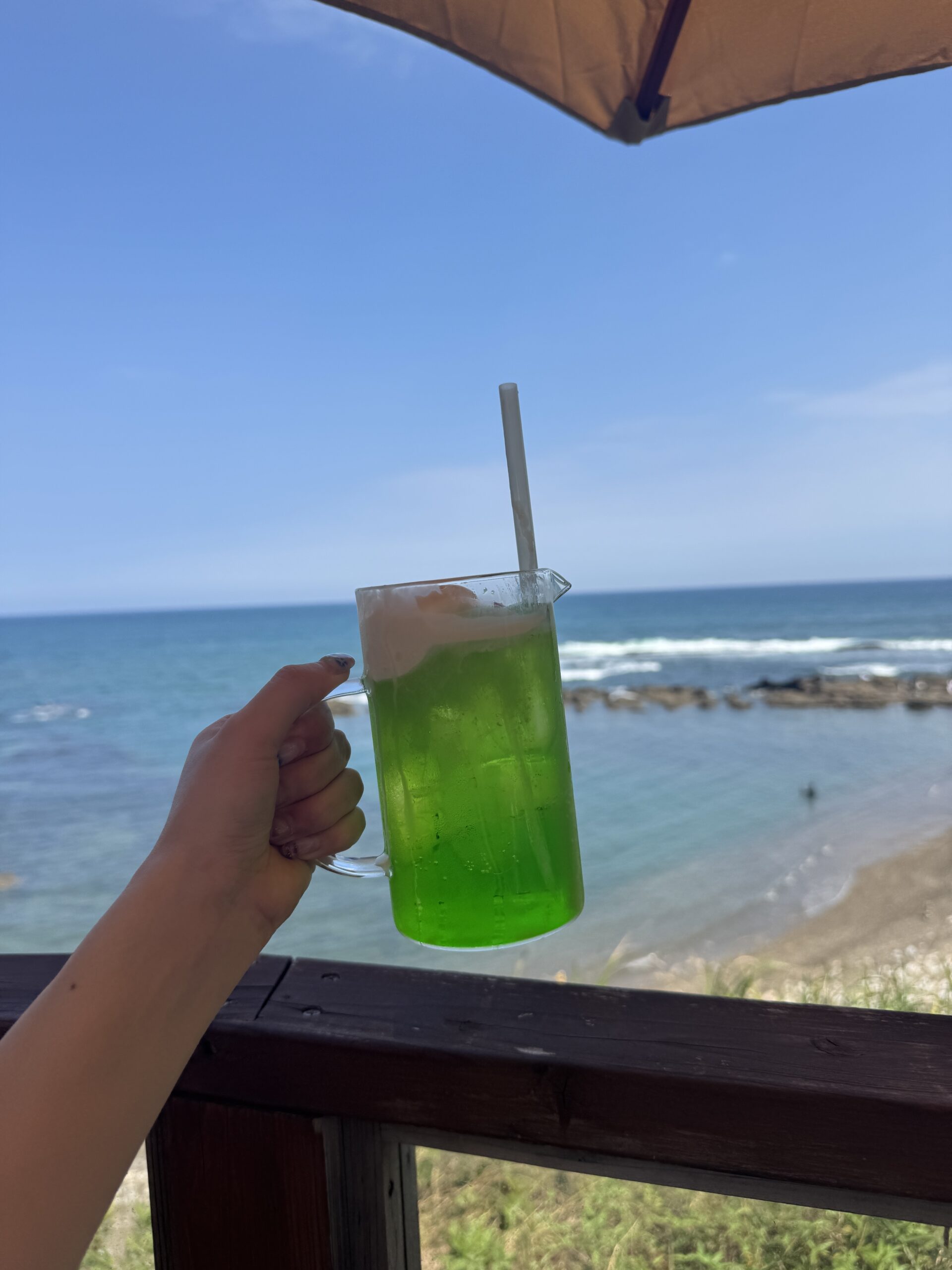 海カフェの席から海を背景に撮った緑色のドリンク