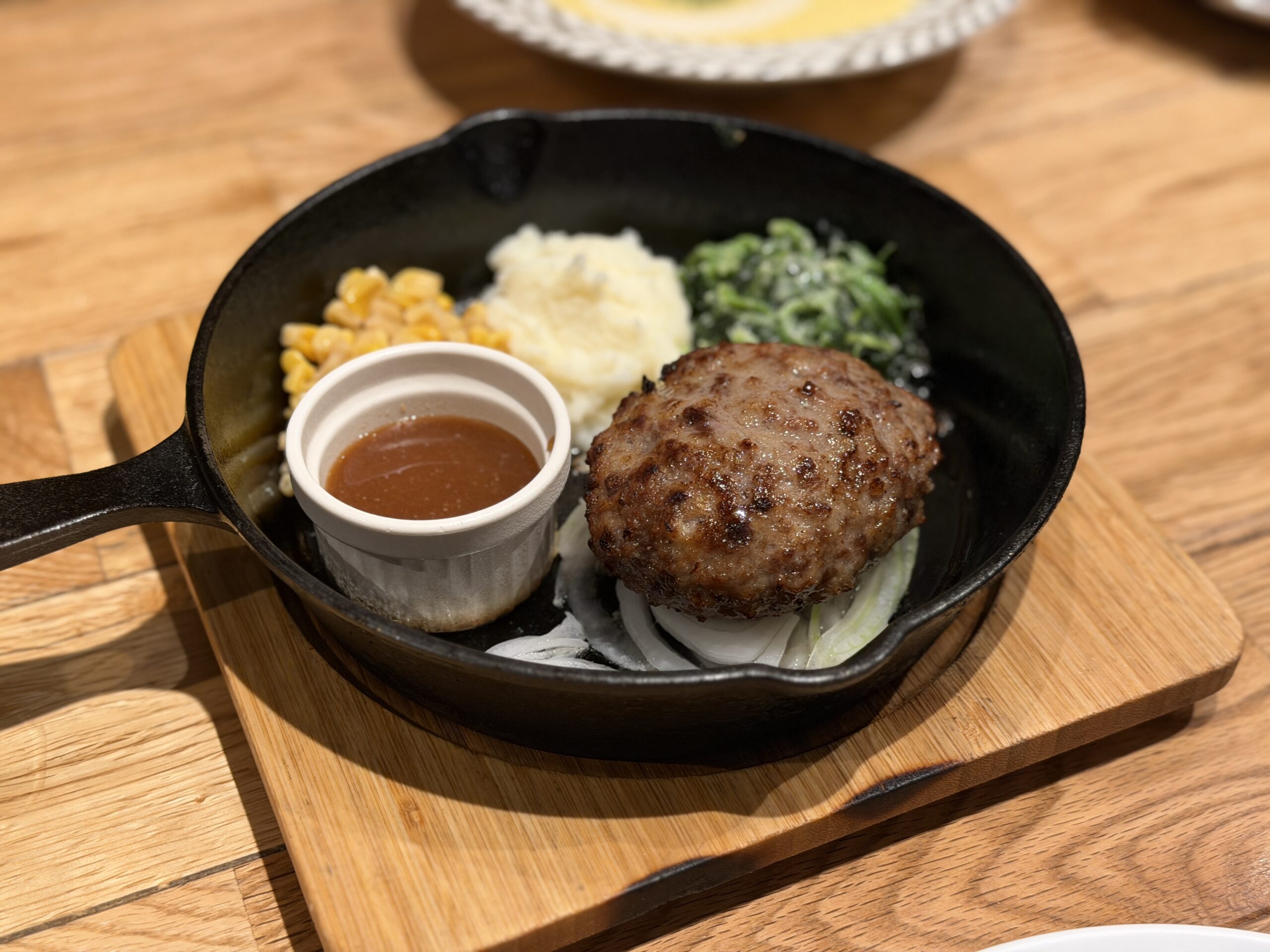 スキレットにのったハンバーグと、別添えのソース、コーンや青菜
