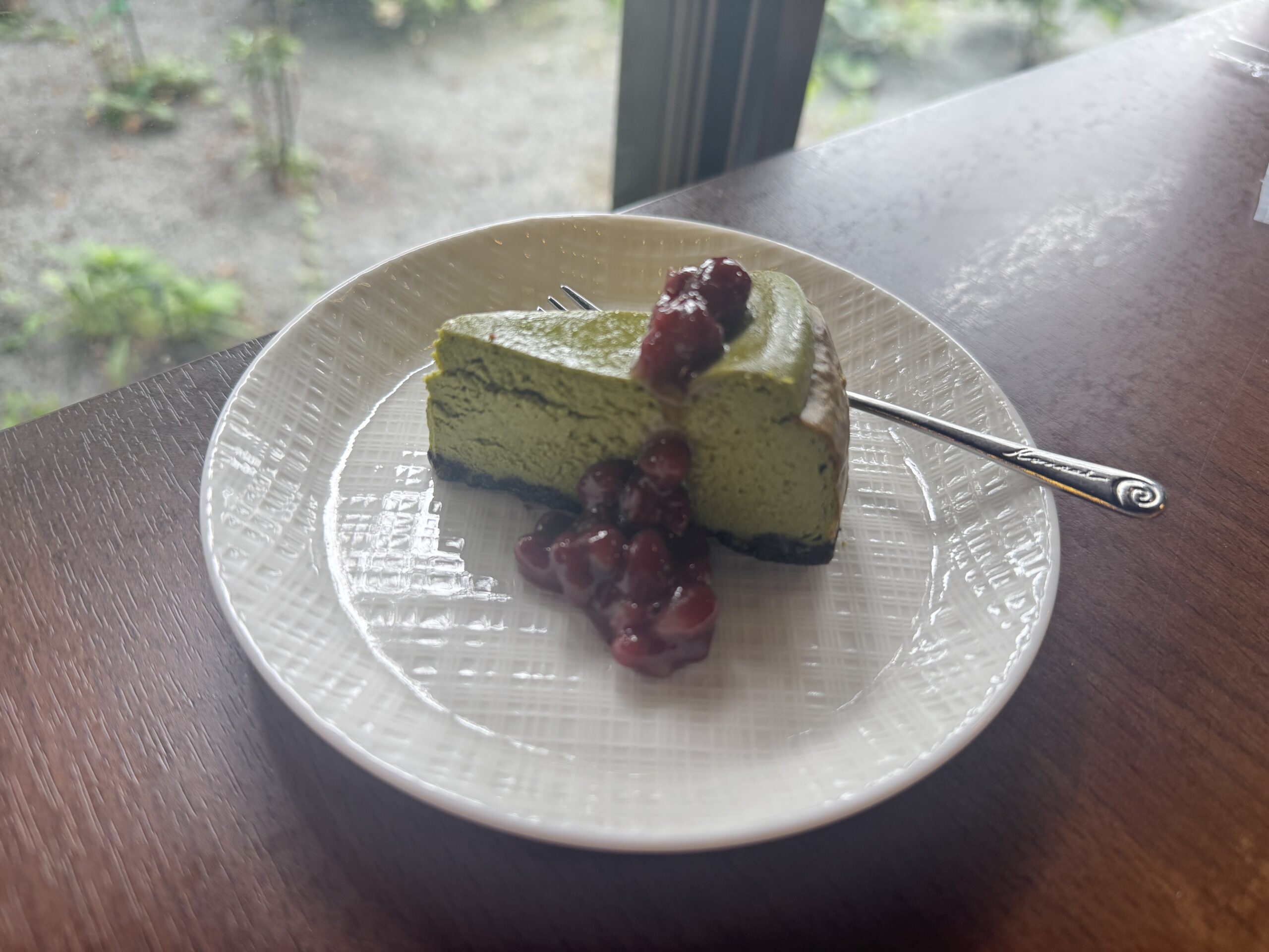 窓辺のテーブルに置かれた、あずきとクリームを添えた抹茶の豆乳チーズケーキ